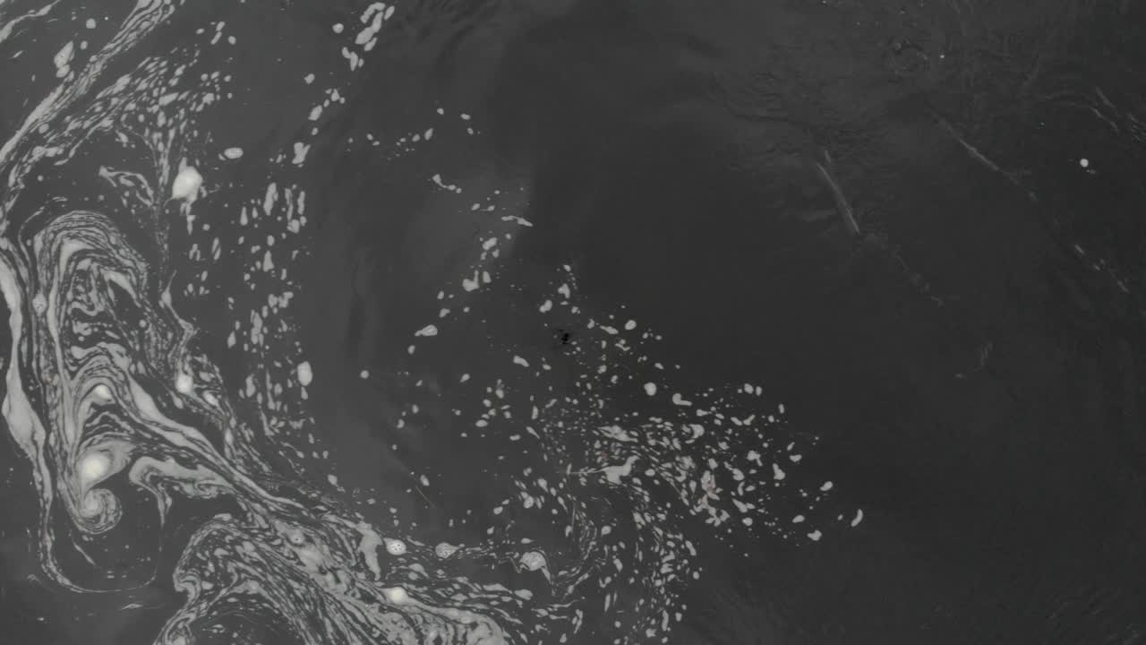 Foamy black water from drone, slowly rising with camera straight down