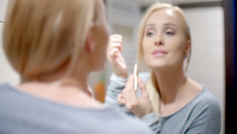 happy woman putting make up in front a mirror