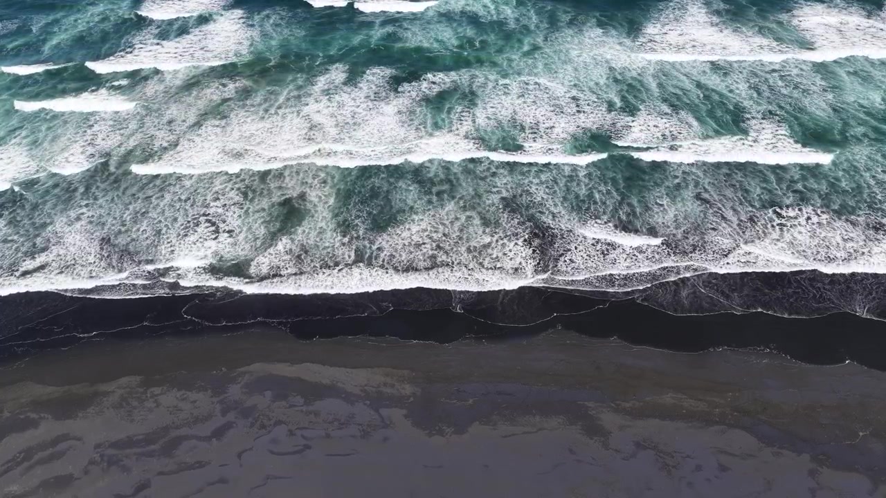 Vista aerea di potenti onde oceaniche che si infrangono su una spiaggia di sabbia nera sull'Isola del Nord della Nuova Zelanda, mostrando surf spettacolare, una costa frastagliata e un paesaggio naturale incontaminato.