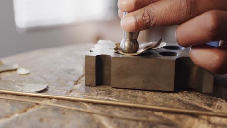 biracial female worker shaping jewellery with hammer in studio in slow motion