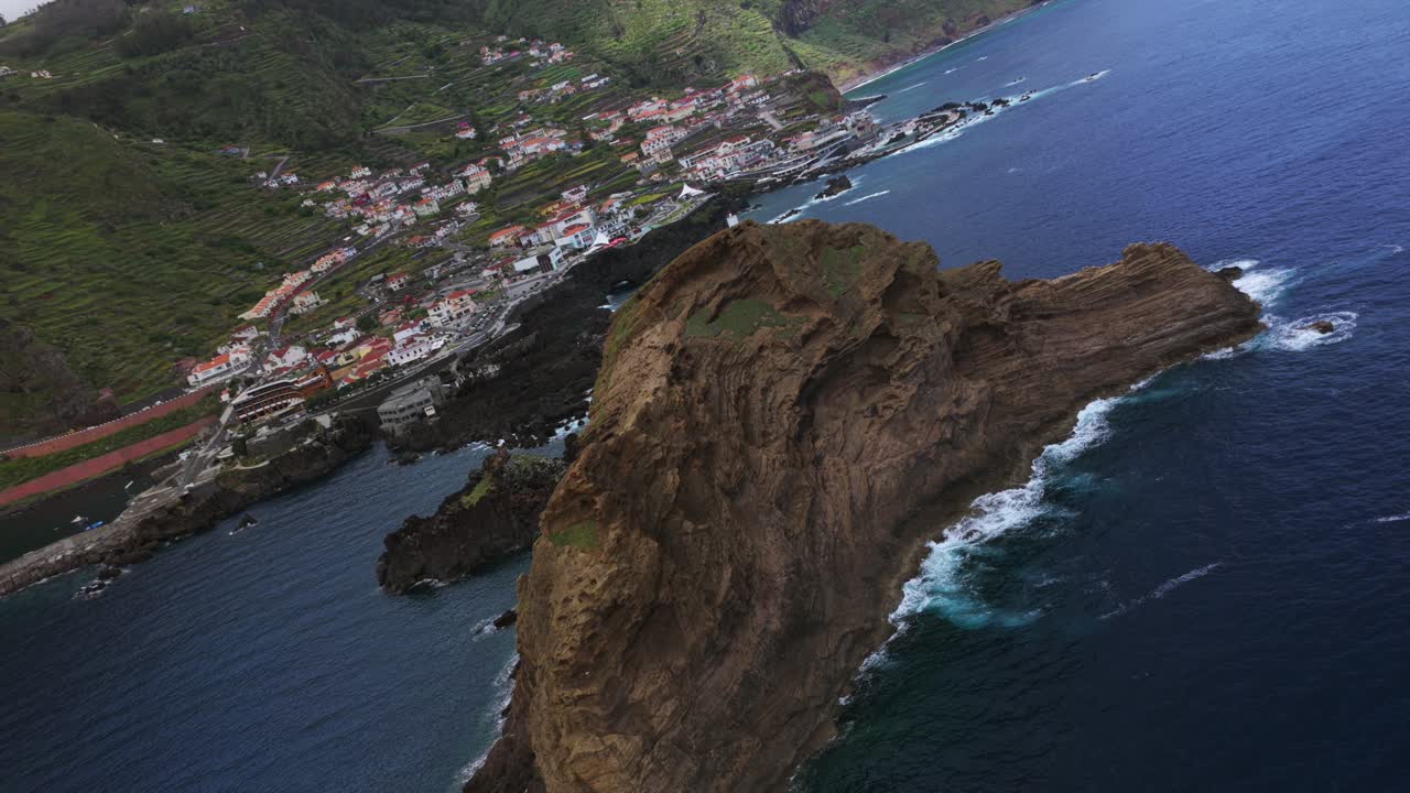 Accidentado islote Ilhéu Mole, formaciones rocosas volcánicas, olas y la ciudad costera de Porto Moniz, Madeira, Portugal. Vista aérea con dron
