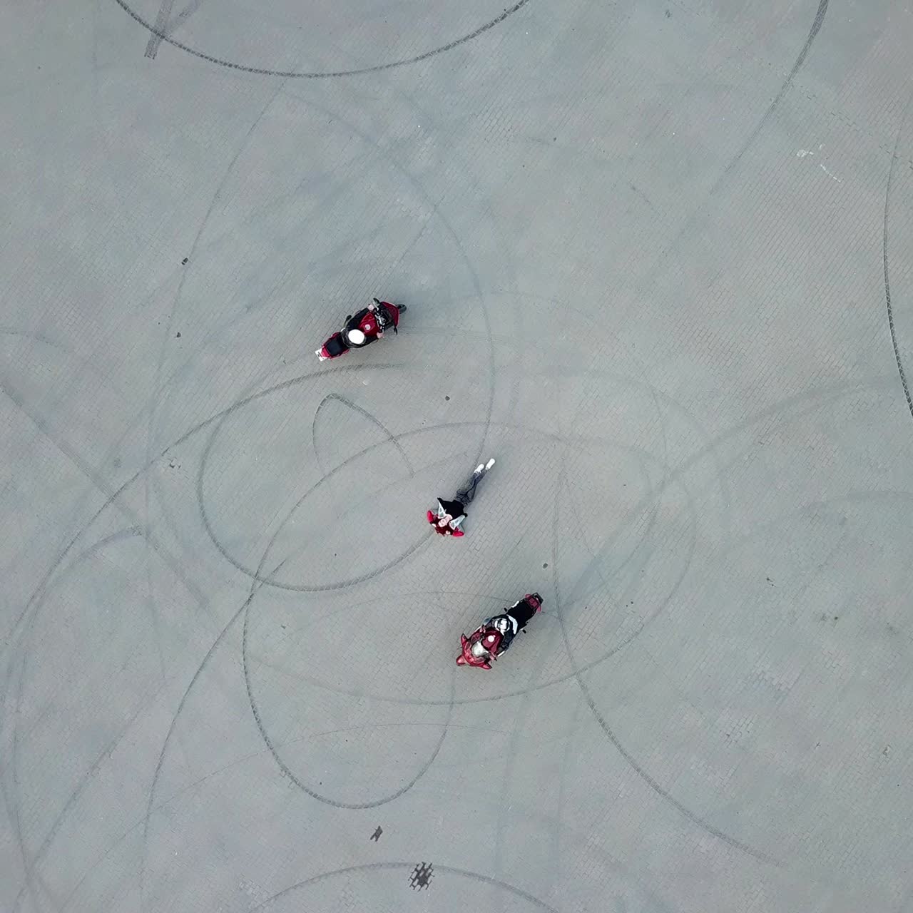 two motorcyclists are riding around woman which is laying on the pavement in the city. Aerial view. Camera motion down