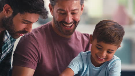 close up of same sex family with two dads and son doing jigsaw puzzle in kitchen at home