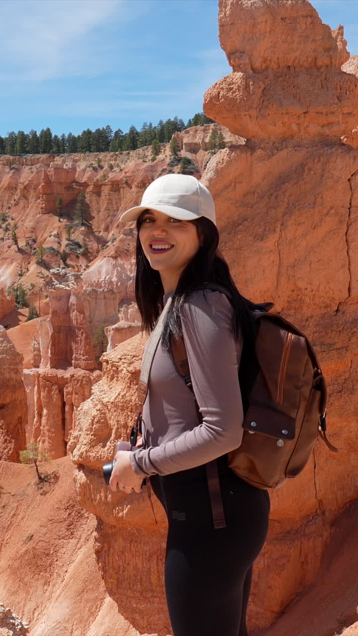 Nuori nainen repun ja kameran kanssa hymyilee Red Rock Canyonissa