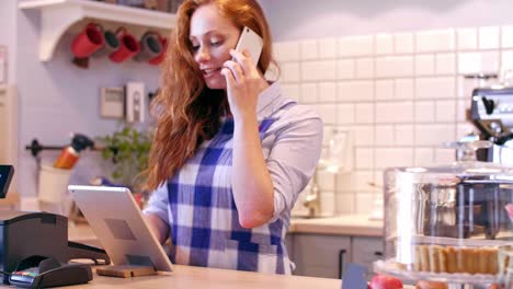 barista hablando por teléfono móvil y usando tableta en una cafetería