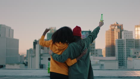 happy-girl-friends-on-rooftop-with-arms-raised-celebrating-friendship-enjoying-hanging-out-together-drinking-alcohol-embracing-freedom-looking-at-urban-city-skyline-at-sunset