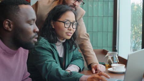 multiethnic team discussing business project on laptop in cafe