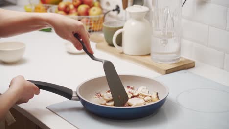 crop faceless woman frying mushrooms and onions in pan on stove