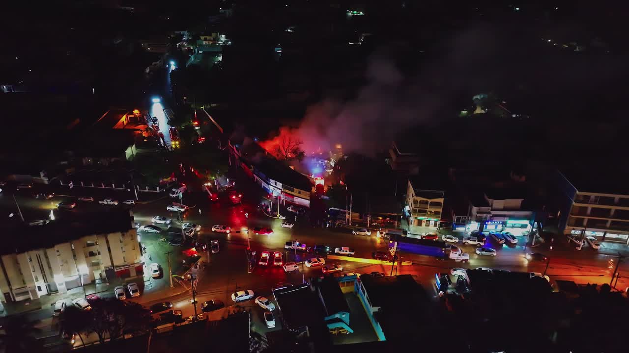 Cinematic aerial view of an urban fire burning amidst illuminated city lights