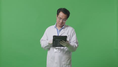 smiling asian man scientist working on a tablet while standing on the green screen background in the laboratory