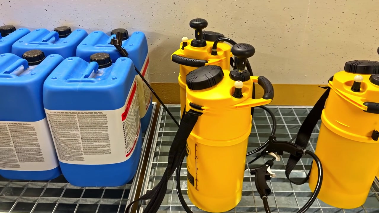 Blue chemical containers and yellow measuring sprayers on a metal shelf for industrial use.