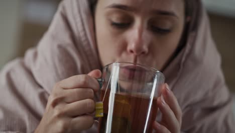 caucasian woman sitting under the duvet with tea at home.