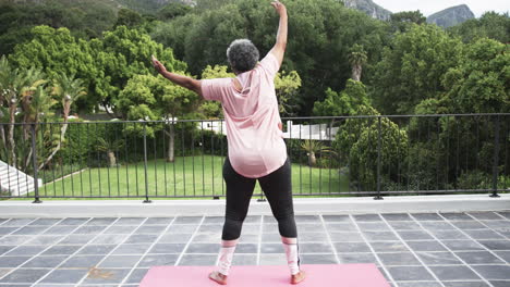 rear view of senior african american woman practicing yoga on balcony, copy space, slow motion