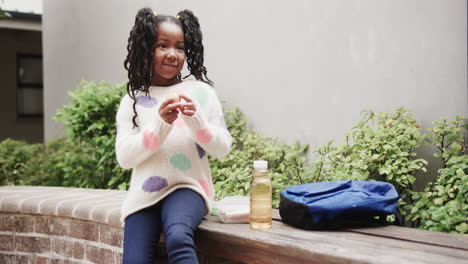 young girl enjoying snack outdoors with backpack and juice, smiling happily, copy space