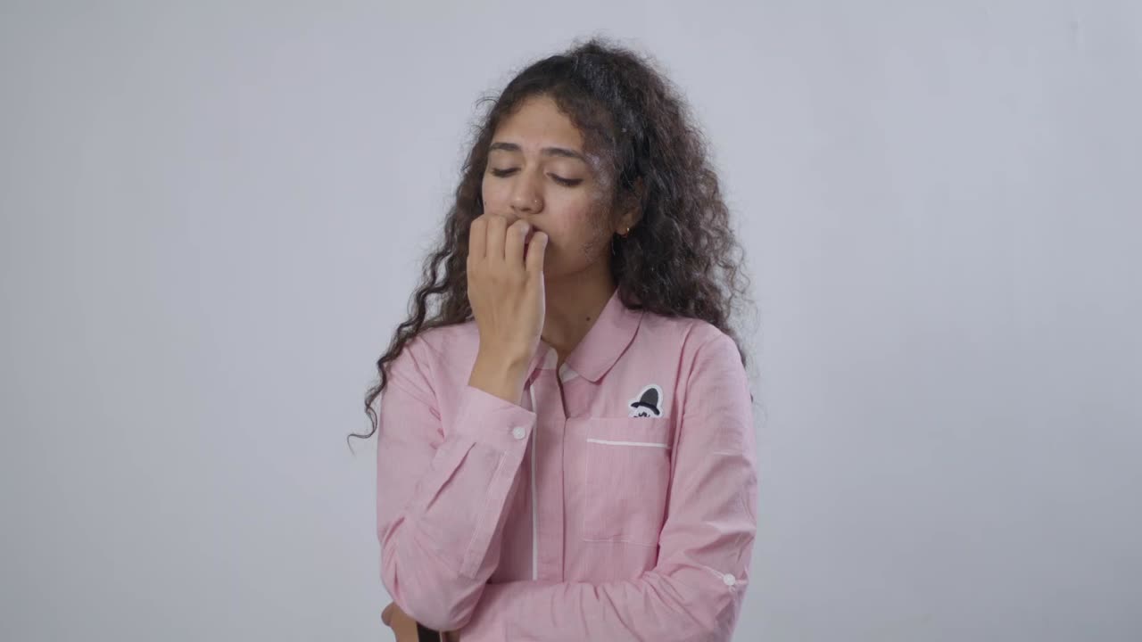 A young South Asian woman with curly brown hair is biting her fingernails, looking worried and anxious