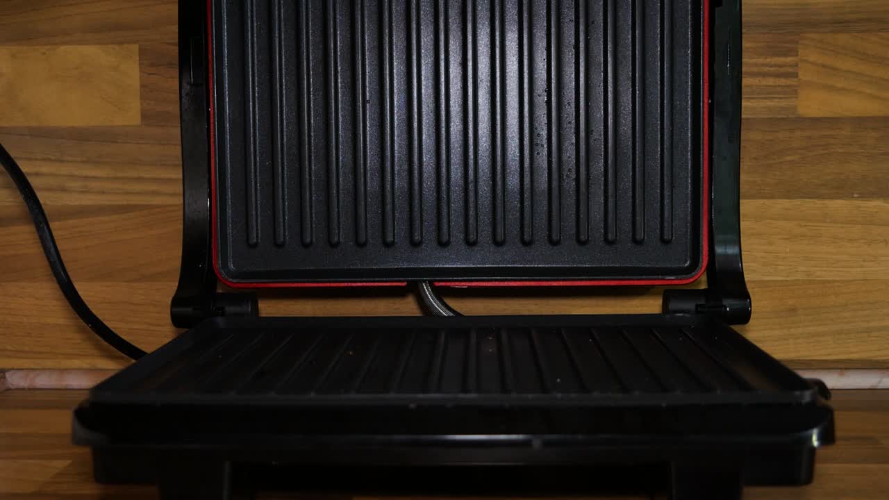 Female home cook putting a delicious sandwich into electric sandwich maker machine. Cooking dinner.