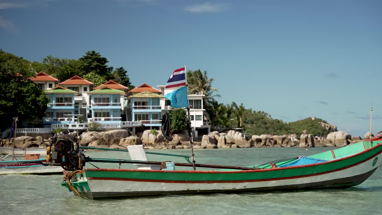 barcos de cola larga de madera vacíos flotando en aguas poco profundas en koh tao, con hoteles de resorts y vegetación exuberante en el fondo