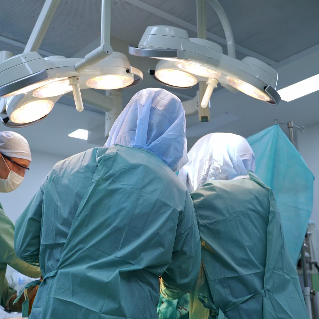 Large surgical team is busy at operational room. Doctors in protective suits stand around the patient on surgery table