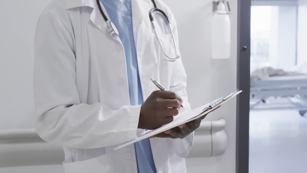 Midsection of african american male doctor taking notes in hospital, slow motion