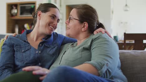 caucasian lesbian couple sitting on sofa, embracing