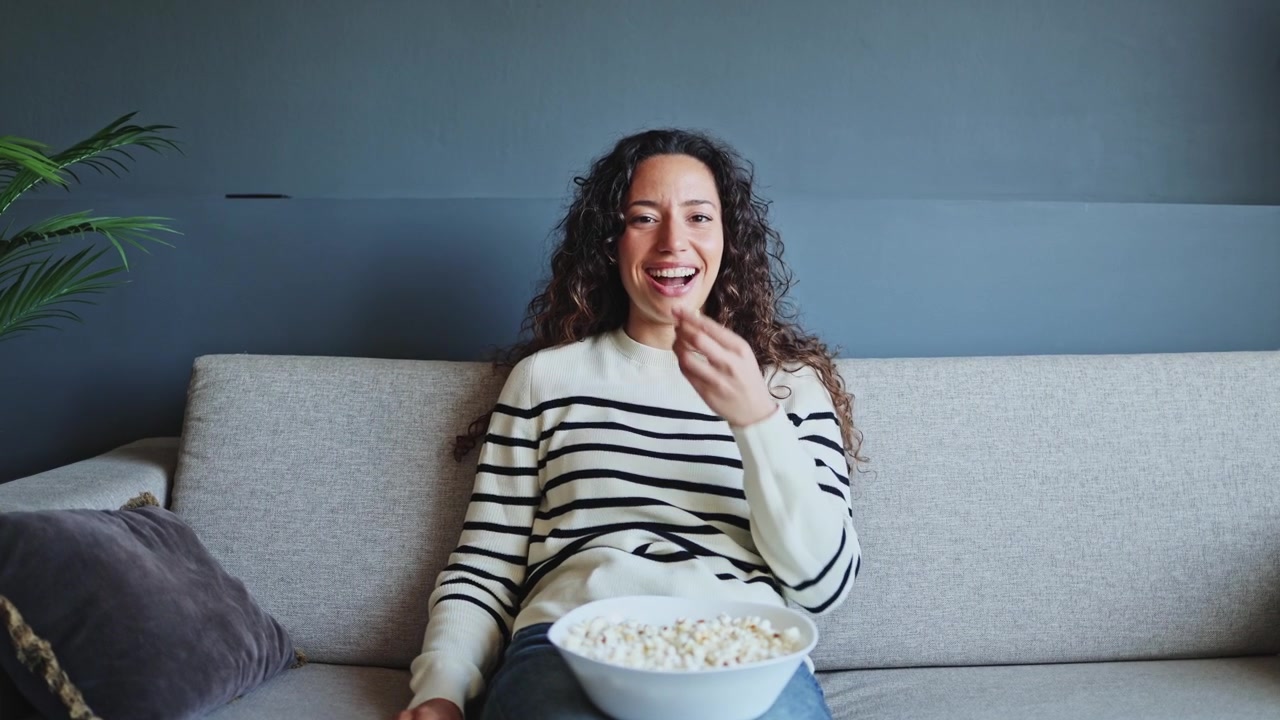 Giovane donna che mangia popcorn mentre guarda la televisione sul divano