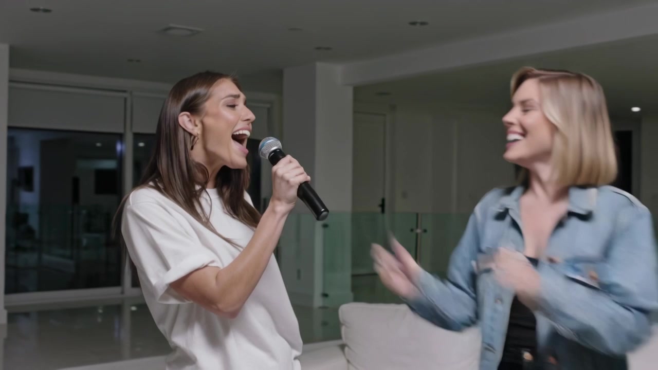 Singing dark-haired woman leading friends in karaoke at home, passing handheld mic for fun