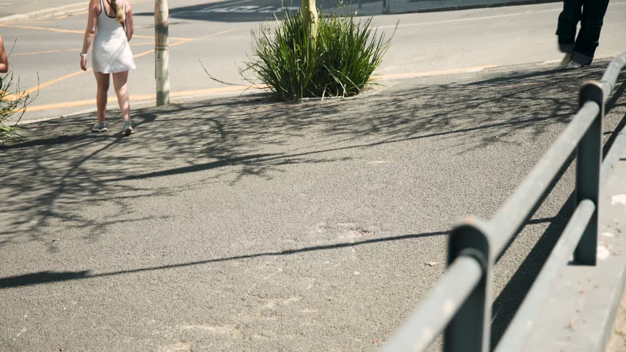 Uomo afroamericano che entra da destra, camminando lungo un vialetto, mentre parla al telefono e porta uno zaino.