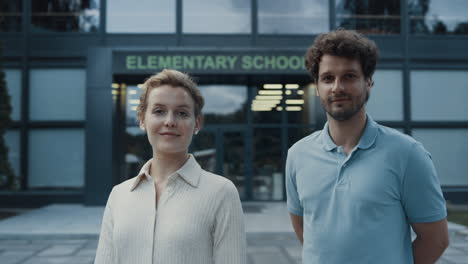 Couple-smiling-teachers-posing-at-elementary-school-entrance.-Education-concept.