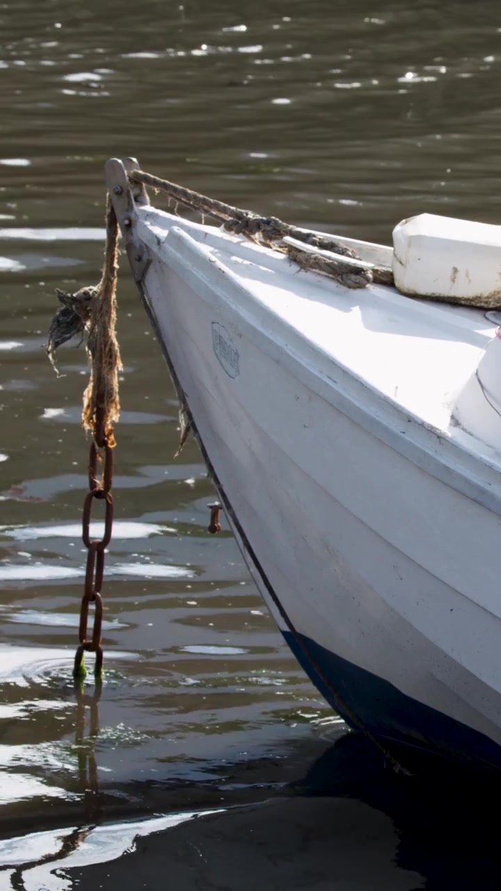 Un'inquadratura verticale dettagliata della prua di una barca bianca e della catena dell'ancora su acqua soleggiata.