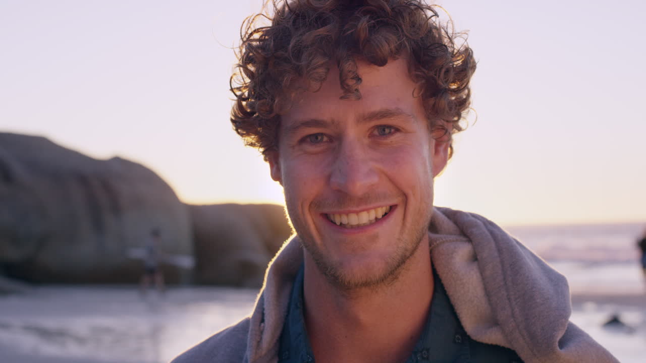 Portrait of attractive man smiling on beach at sunset in slow motion