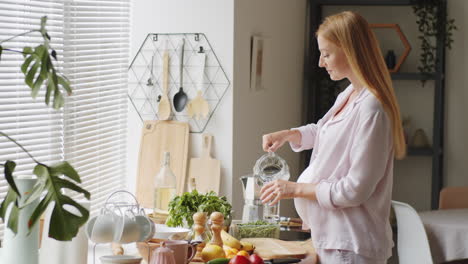 pregnant woman drinking water in kitchen