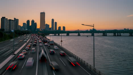 Paisaje-Al-Atardecer-De-Rascacielos-Vista-Desde-El-Puente-Hangangdaegyo,-El-Edificio-63-Y-El-Ifc-En-El-Distrito-Financiero-De-Yeouido,-Timelapse-Del-Tráfico-En-La-Autopista-Olímpica-Durante-La-Hora-Pico-En-El-Crepúsculo---Estático