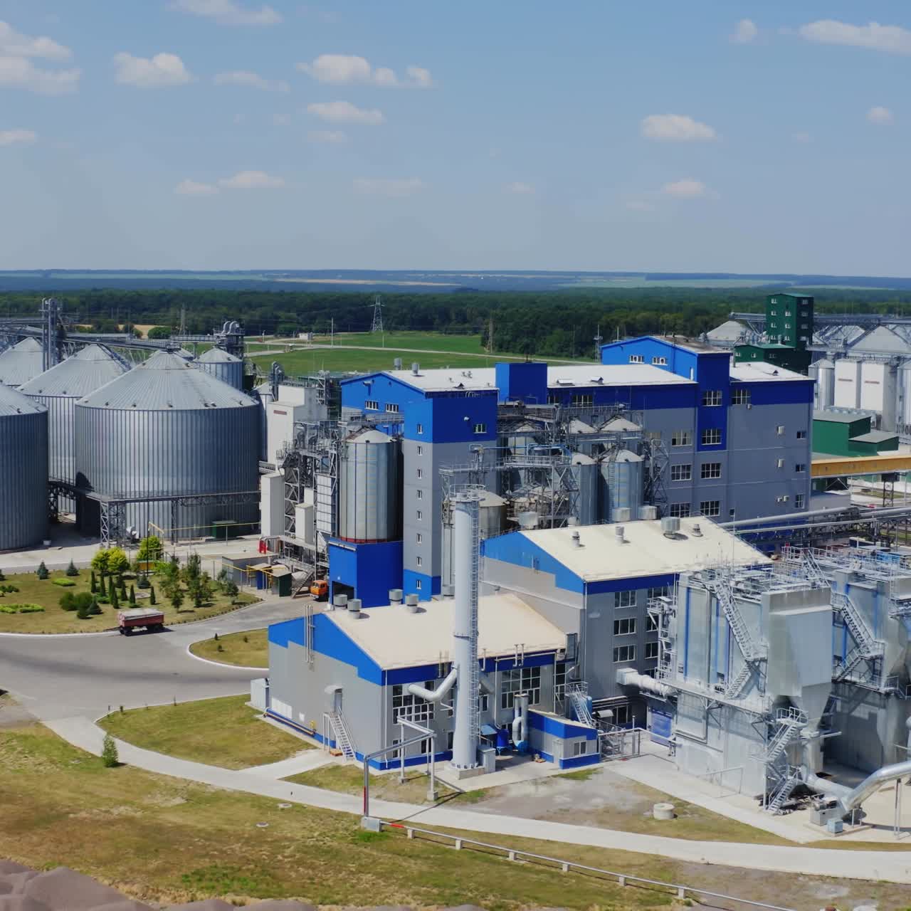 Exterior of modern plant on field. Modern large granary for agro-processing products. Large metal silos. Elevators on factory in sunny day.