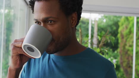 relaxed biracial man drinking coffee, smiling and looking into distance