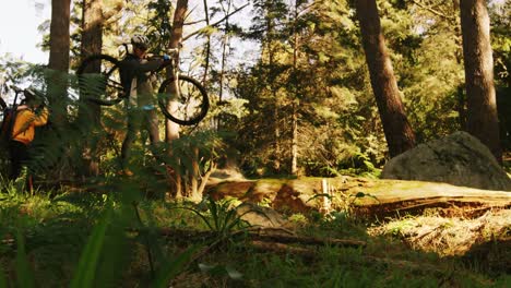 Mountain-biking-couple-carrying-bicycle-while-walking-on-a-log