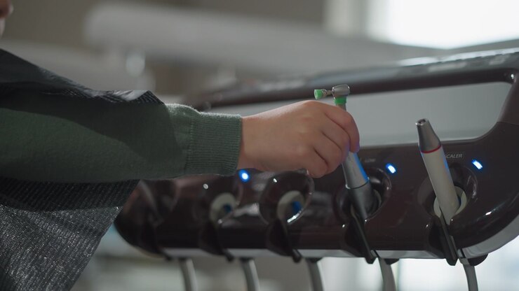 Close up of man hand selecting and holding dental instruments from organized tray in soft lighting. arm extends towards various tools including scalers with blue indicator lights suggesting