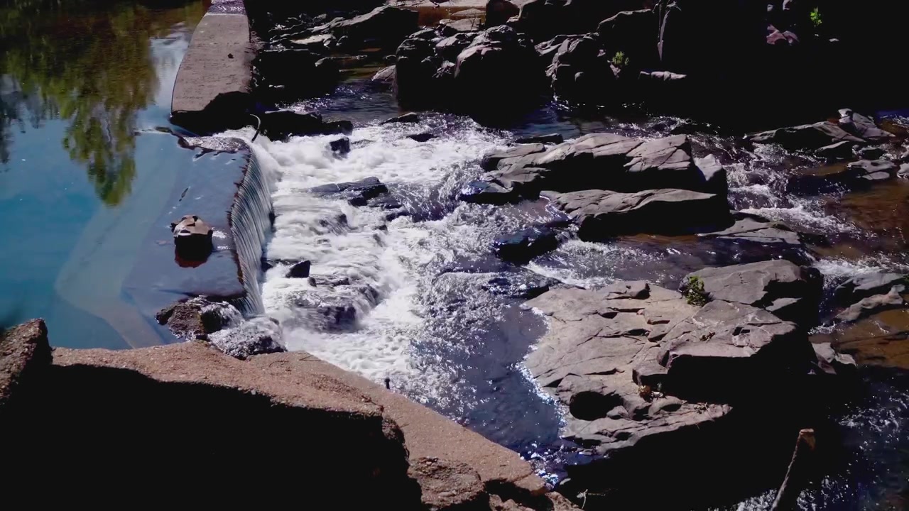 Água Impetuosa Sobre o Histórico Vertedouro de Marble Creek no Missouri Descrição: Uma vista de ângulo elevado que capta a água em cascata sobre o vertedouro de concreto e revolvendo-se pelos desfiladeiros vulcânicos e acidentados