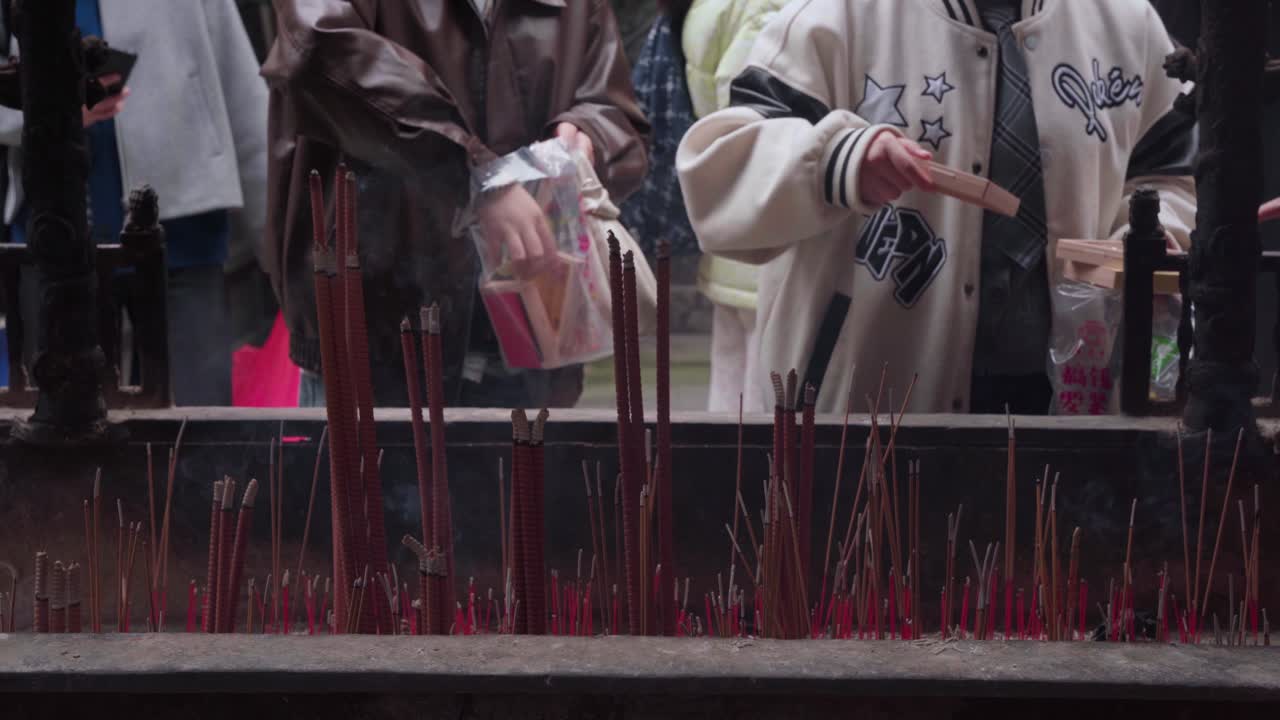 Plan fixe rapproché de visiteurs tenant une petite boîte de divination en bois au-dessus d'un grand brûle-encens pour absorber la fumée d'encens montante lors d'un rituel bouddhiste traditionnel au temple Luohan à Chongqing.