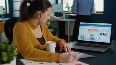 portrait of startup employee analyzing financial data comparing paper with charts with statistics on laptop