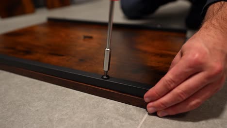 male hand screwing a screw in a wooden table to assemble kitchen furniture