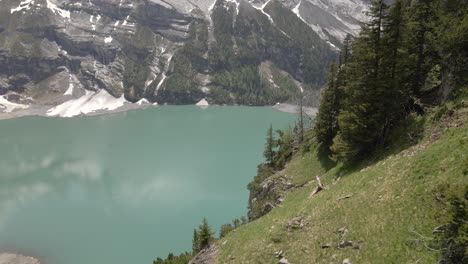 mountain reflecting in the water of the oeschinensee lake while flying past a steep overgrown hill of fir and pine trees
