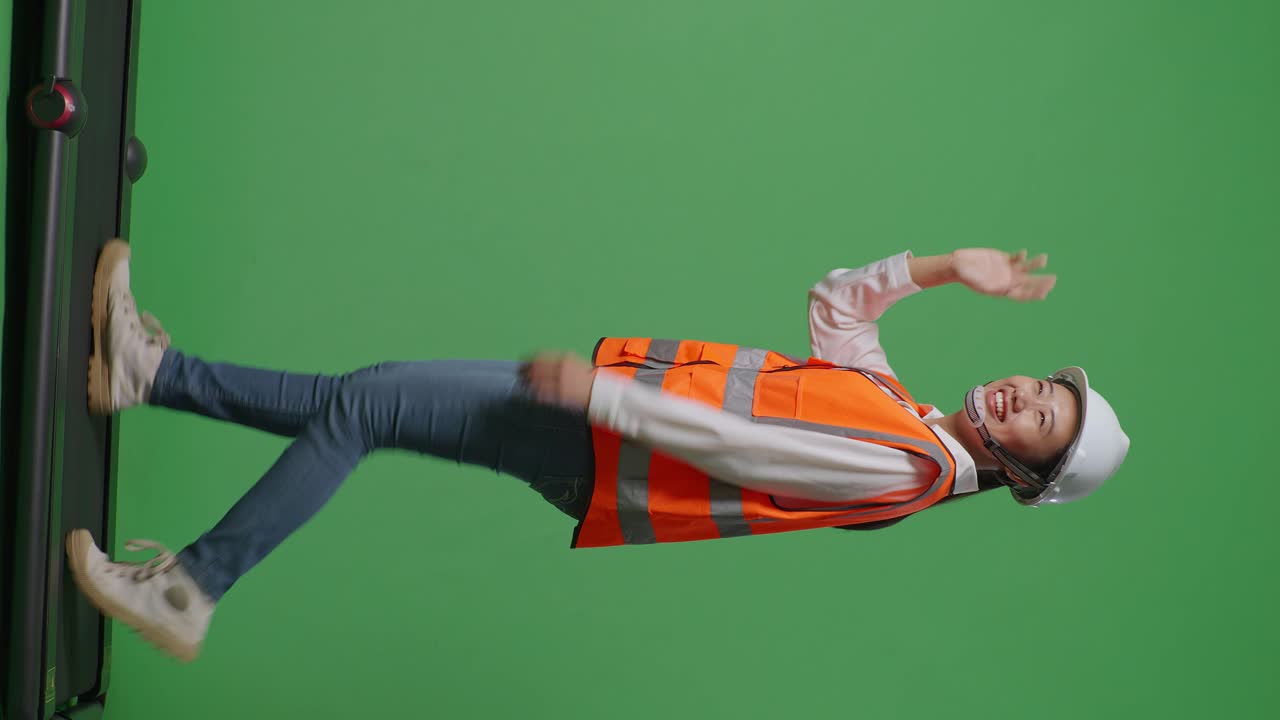 안전 헬을 입은 아시아 여성 엔지니어가 녹색 화면 배경 스튜디오에서 는 동안 손을 흔들고 있습니다.