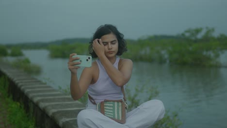 Una-Joven-India-Se-Toma-Selfies-Alegres-Junto-A-Un-Río-Sereno,-Creando-Una-Hermosa-Composición-De-Su-Vibrante-Energía-Joven-Y-El-Tranquilo-Telón-De-Fondo-Natural