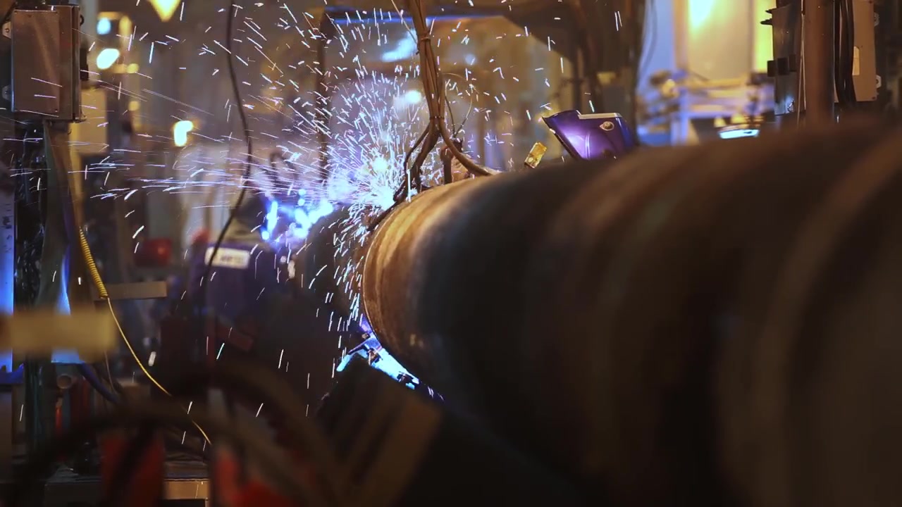 Close industrial workshop scene shows bright welding sparks flying around large metal pipe and machinery for manufacturing engineering repair and labor concepts