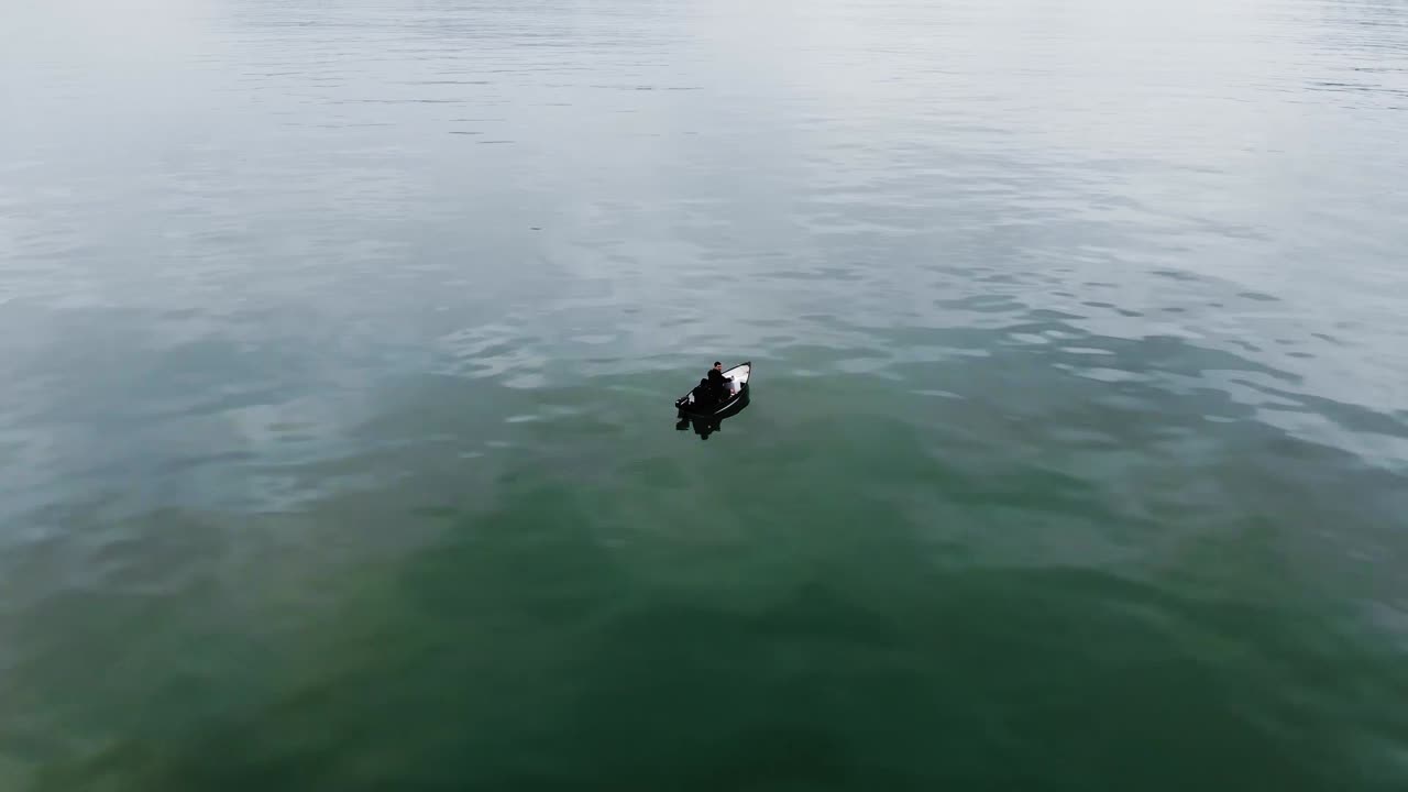 햇빛 아래 고요한 호수 물에서 휴식을 취하는 작은 보트에 있는 두 사람을 보여주는 공중 전망
