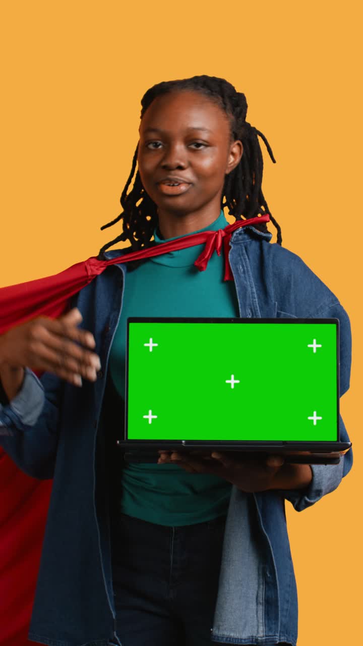 Giovane supereroina afroamericana che tiene in mano un laptop con green screen