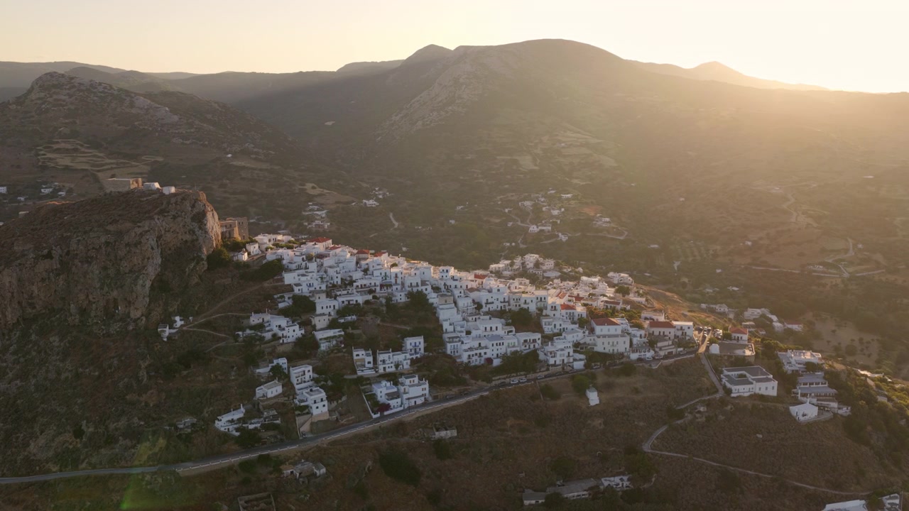 Luce dorata del tramonto che illumina un tradizionale villaggio bianco costruito su un ripido fianco di montagna nelle isole greche. Rivelando lo splendido paesaggio e l'architettura cicladica da una prospettiva aerea