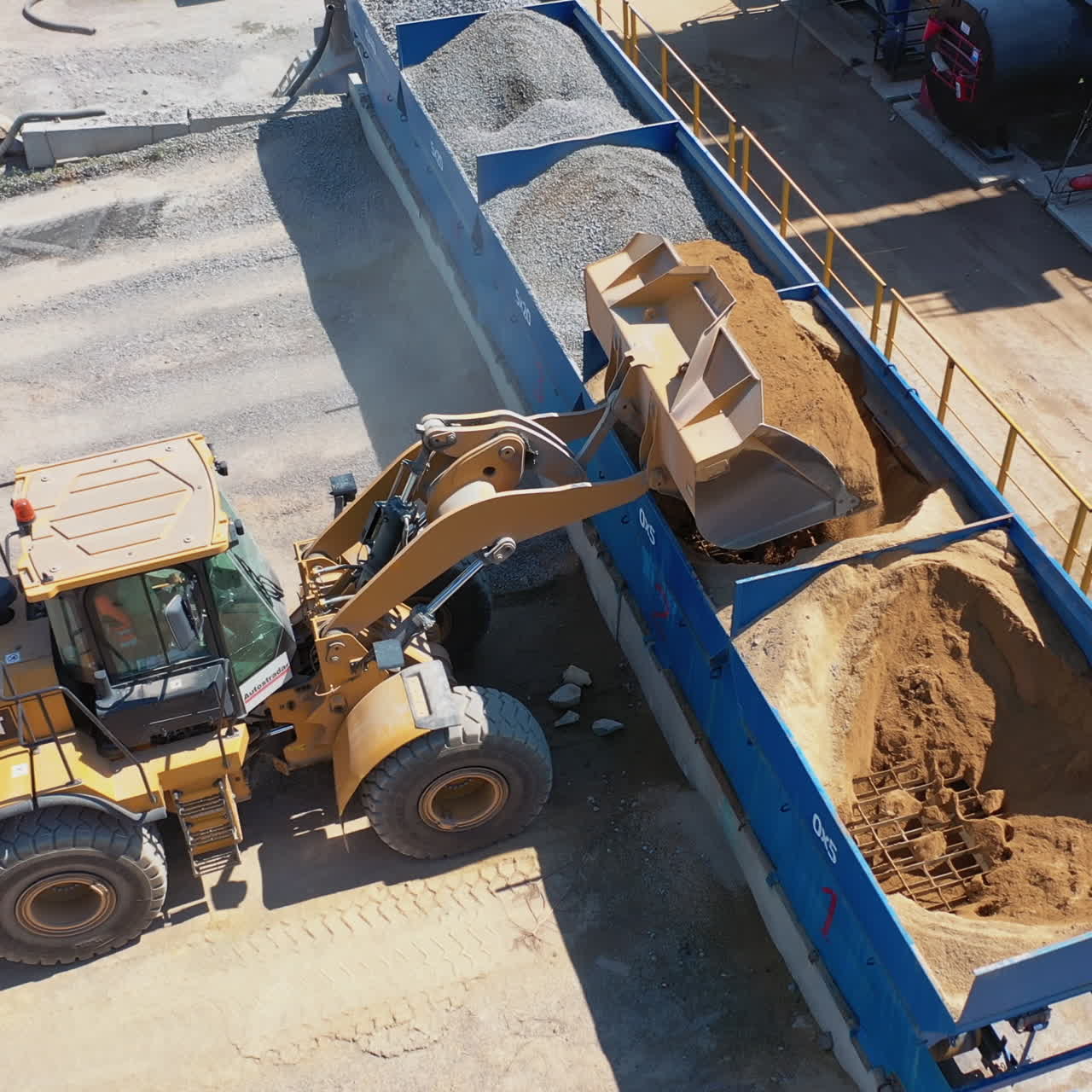 Excavator on the territory of asphalt manufacture outdoors. Modern excavator pouring out sand from bucket into a special tank. Top view.