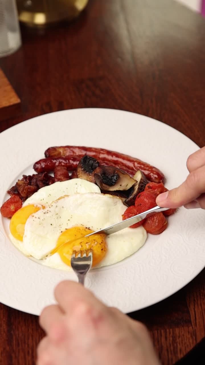 Persona che taglia un uovo fritto con tuorlo filante su un piatto per la colazione