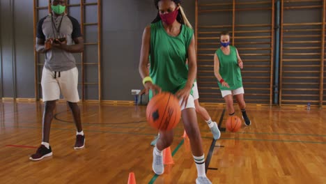 Diverse-female-basketball-team-and-coach-wearing-face-masks-practice-dribbling-ball